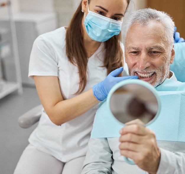 An older man admiring his new dental implant in a hand mirror