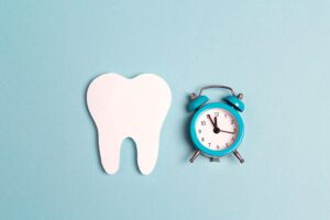 Large cut-out tooth next to a toy alarm clock on a pale blue background